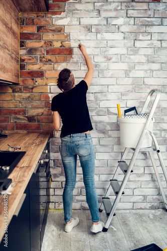 woman renovating a kitchen, painting a brick wall white © kerkezz