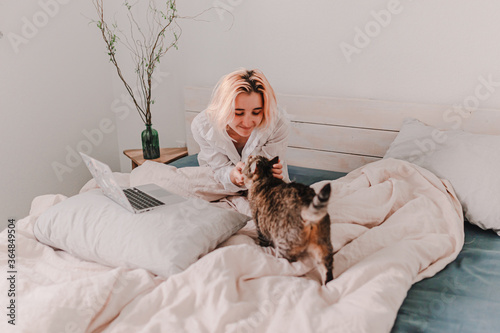 Young woman is relaxing in bed. Day off. Bedtime. Early morning light. White, beige, grey. Light and bright. Morning ritual. Apartment lifestyle living. Cozy bed linen. Soft pillow and comforter.