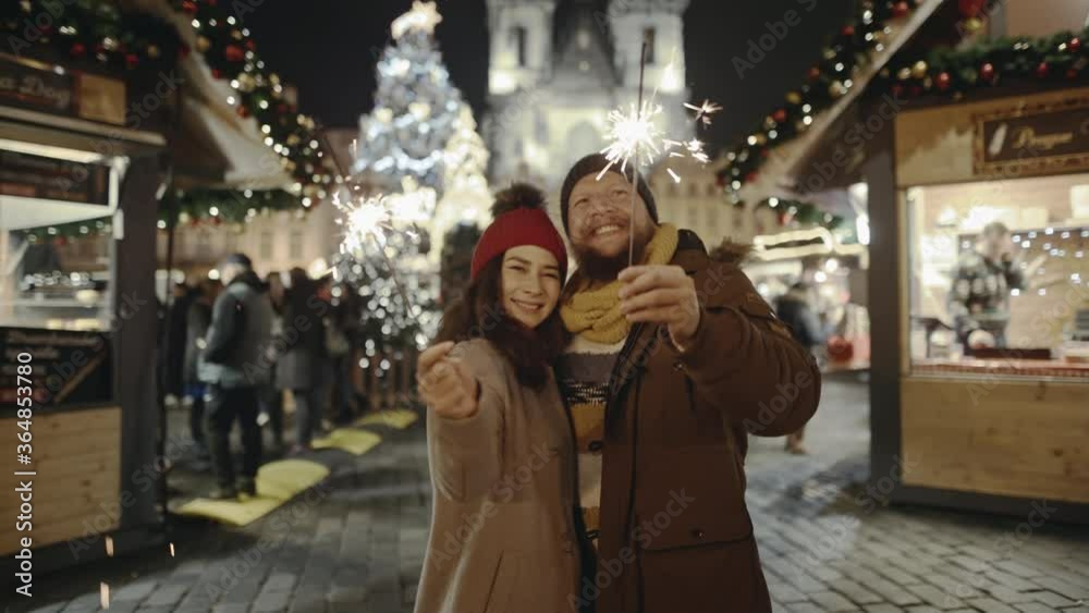 Lovers travelling to Europe at the height of Christmas holidays. Romantic couple in love hugging and burning the sparklers at festive street fair. Sweethearts kissing in the centre of old city. Lovers travelling to Europe at the height of Christmas holidays. Romantic couple in love hugging and burning the sparklers at festive street fair. Sweethearts kissing in the centre of old city.