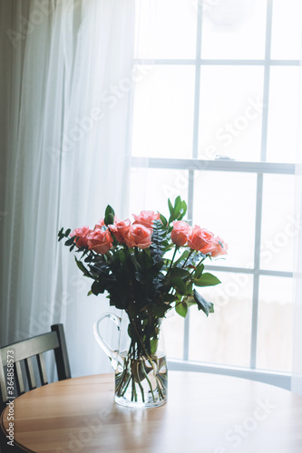 Bouquet of beautiful roses on wooden table near the window at modern kitchen