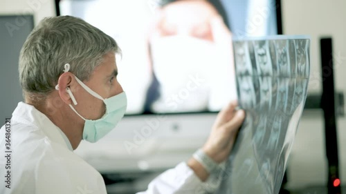 Video call in coronavirus times. Doctor wearing mask and examining xray scan visiting woman at home. Slow motion photo