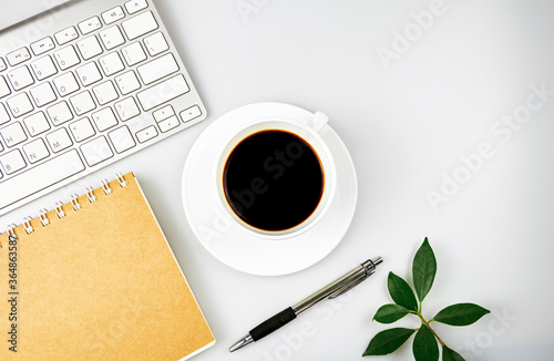 White office desk table. Workspace with keyboard, notebook, office supplies, pen, green leaf, and coffee cup on white background. Top view with copy space, flat lay.