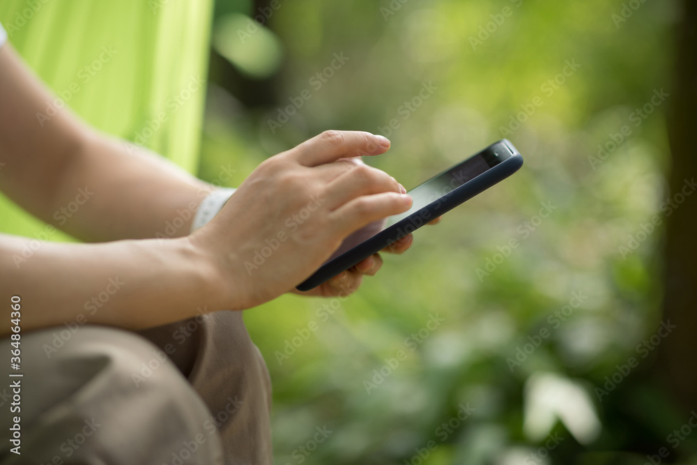 Relaxing in hammock hand using smartphone in tropical forest