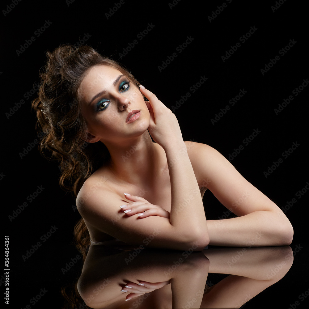 Fototapeta premium Beauty portrait of young woman sit at the black table. Brunette girl with long hair and evening female makeup on black background