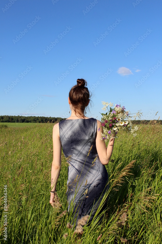 Girl holding wildflowers in her hands behind her back Girl holding wildflowers in her hands behind her back