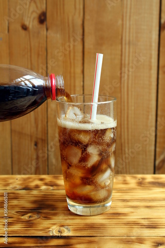 Pour cola from a bottle into a glass with ice photo