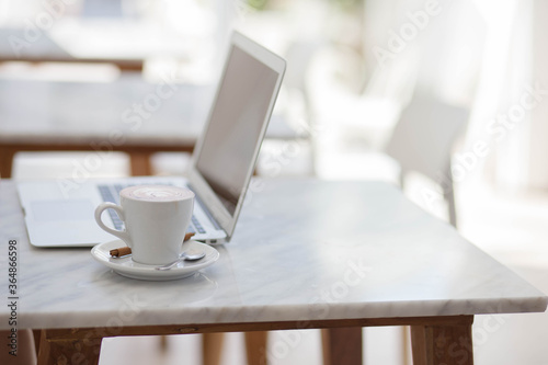 cup of coffee on table with laptop in cafe background.