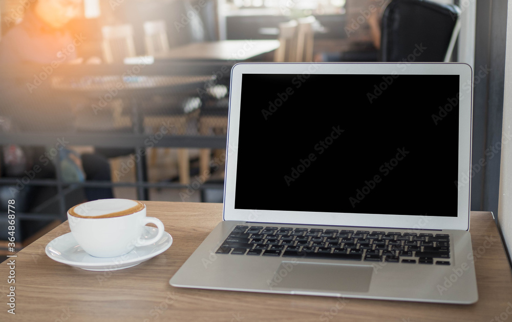 Fototapeta premium Modern technology and communication concept. Close up view of open notebook computer, and mug of cappuccino resting on wooden table,