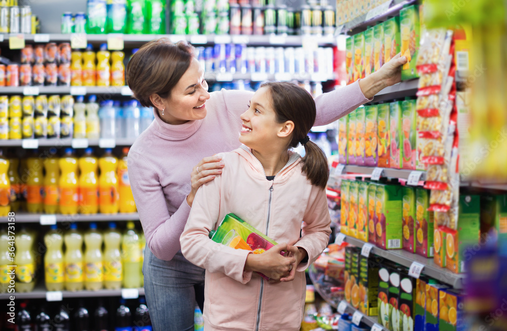 Cheerful positive smiling female shopper with teenage daughter searching for beverages in supermarket