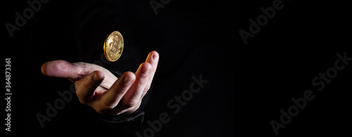 Hand throwing golden bitcoin in the air on black background - narrow banner with copy space