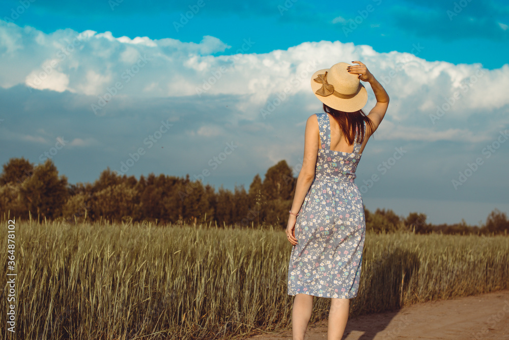 A girl walks in the summer in a field where rye or wheat grows. She is holding a hat in her hands. 6