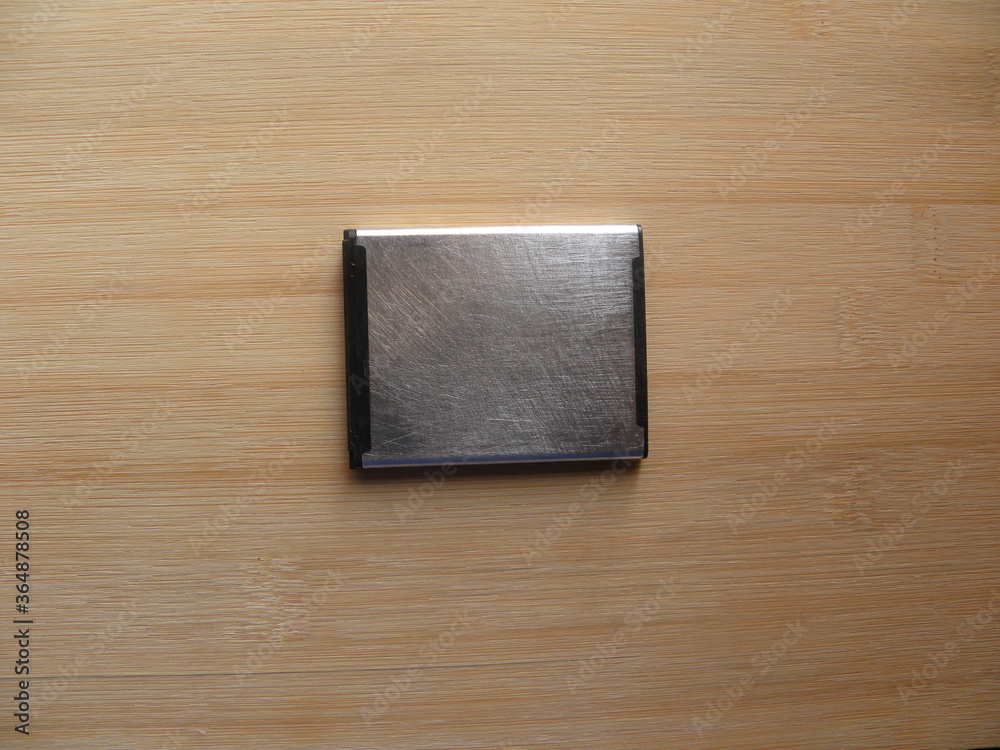 Silver internal battery of smartphone kept on wooden table Silver internal battery of smartphone kept on wooden table