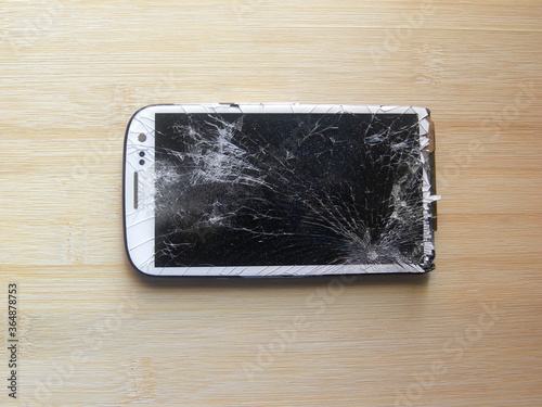 Broken and damaged white color cell phone kept on wooden table