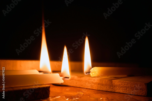 White Candles Burning in the Dark with lights glow, The burning candle's flame in the dark background, a symbol of the Christian faith, Candles Burning in the Dark with lights glow.