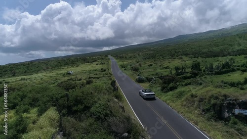 Convertible drives down east Kaupo road towards Kula Maui Hawaii. Aerial drone footage. Green beautiful coastline.  photo