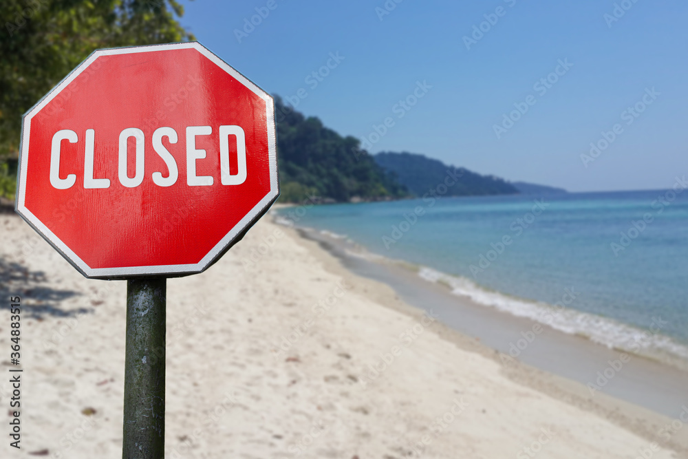 Red closed sign on beach background. Closed facilities because of corona virus. COVID-19 pandemic quarantine.