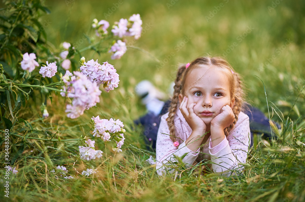 The little girl lies on the grass and holds her head with her hands. Girl makes different facial expressions The little girl lies on the grass and holds her head with her hands. Girl makes different facial expressions