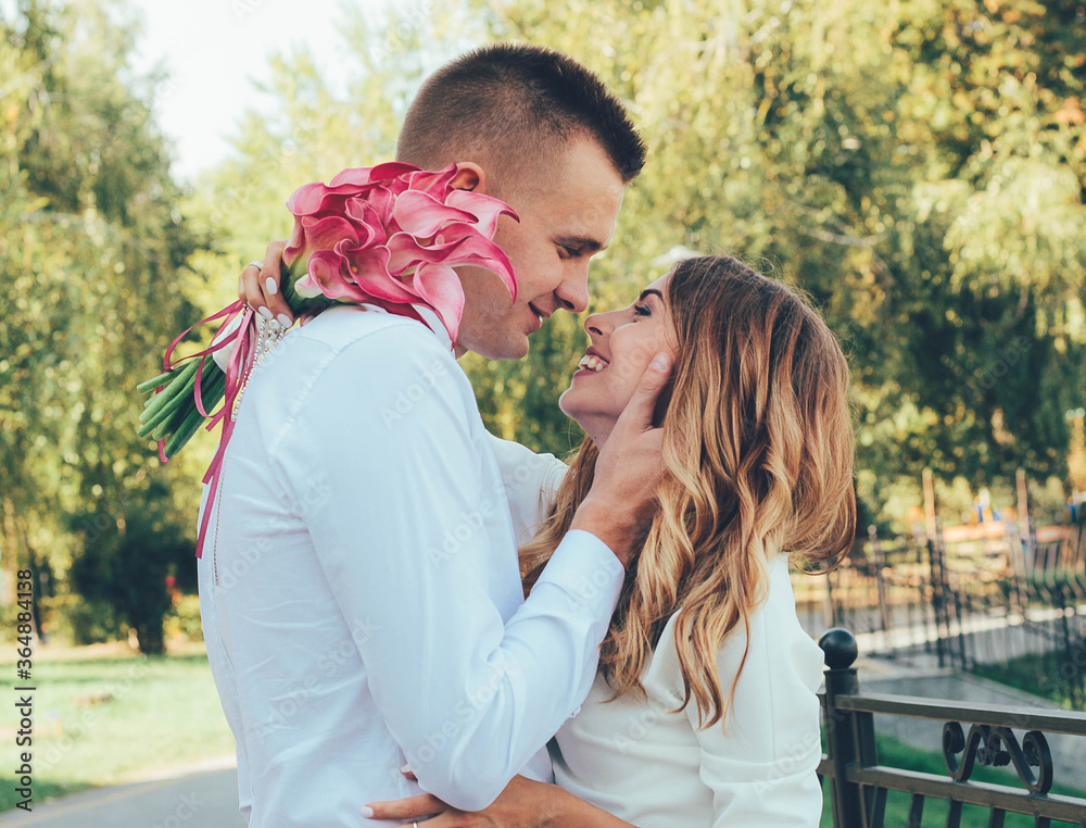 Fototapeta premium The guy kisses the girl in the park, the guy hugs the girl by the face, the couple kisses in the park