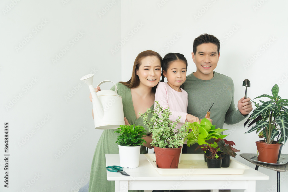happy asian family father mother and daughter with small tree in flower pot, home gardening concept.