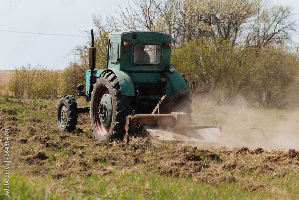 Fototapeta premium An old blue tractor plows a field and cultivates the soil. Agriculture.