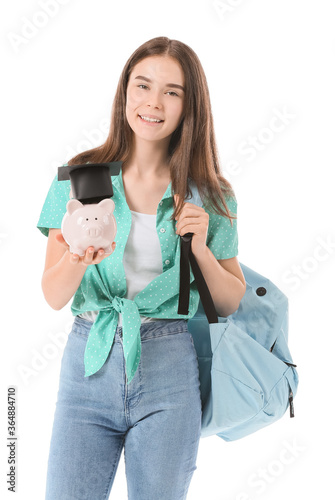 Smiling teenage girl holding piggy bank with graduation cap, education saving...