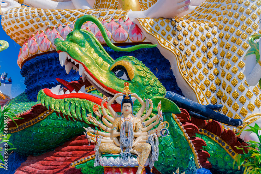 Religious statue in a Buddhist temple in Thailand. The many-armed statue of the God on the background of the green dragon. Religions of Southeast Asia. Tourist destination of Thailand. 