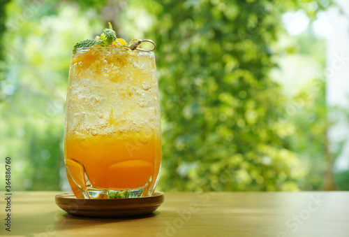 A glass of orange juice mixing with soda. The icy drink is on a wooden table with green garden in blurred background.  Summer, refreshment and beverage ideas.