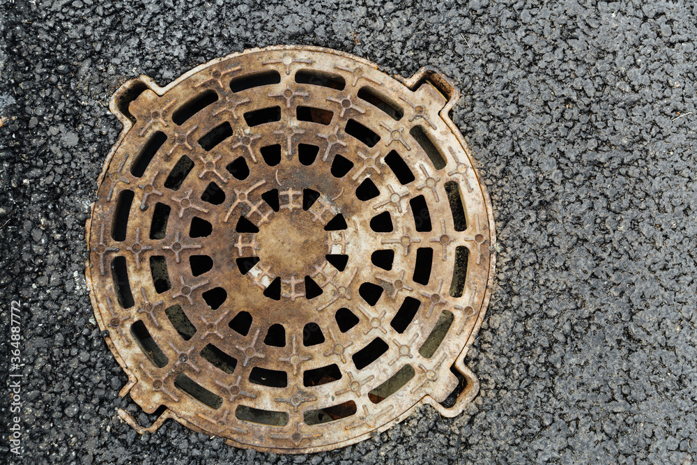 Closed sewer manhole, which is located on the sidewalk. There are holes in the manhole cover. Close up