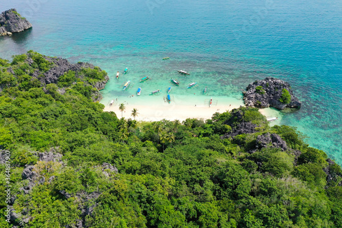 Rocky island with a white sandy beach, top view. Aerial top view of ocean waves, beach and rocky coastline and beautiful forest. Caramoan Islands, Matukad , Philippines.