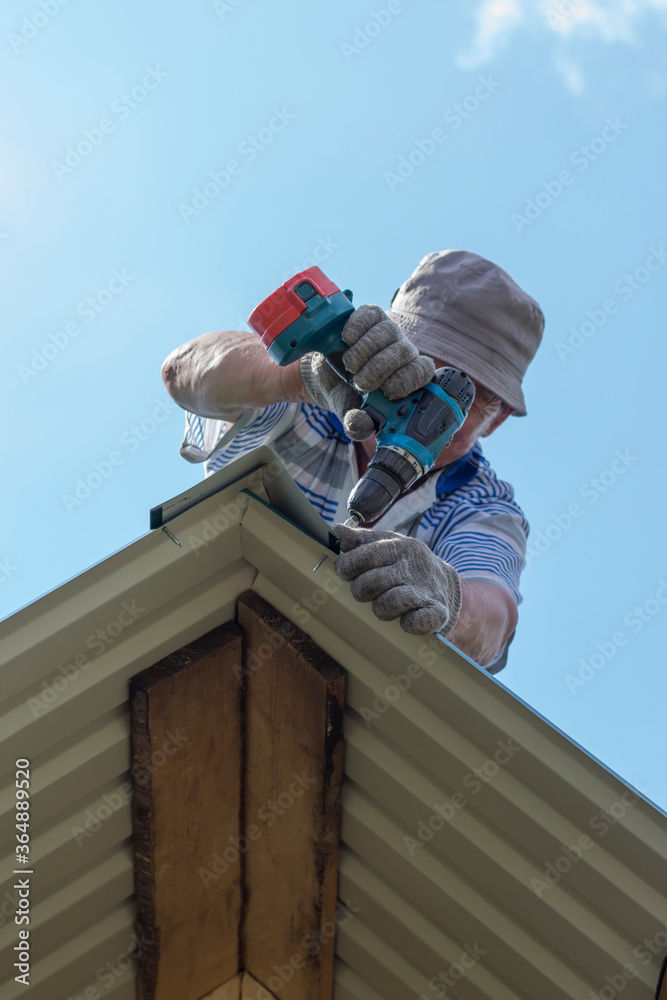 a man works on the roof, attaches the visor with a drill and screws