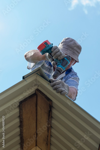 a man works on the roof, attaches the visor with a drill and screws © Irina