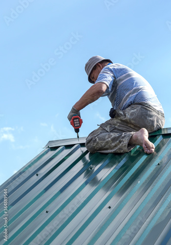 a man sitting working on the roof, attaches the visor with a drill and screws
