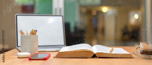 Study table with opened book, mock up laptop, smartphone, stationery and coffee cup