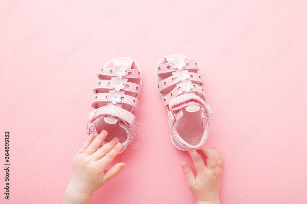 Baby hands touching sandals on light pink floor background. Pastel color. Closeup. Point of view shot. Top down view. Baby hands touching sandals on light pink floor background. Pastel color. Closeup. Point of view shot. Top down view.