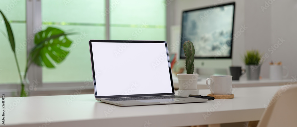 Fototapeta premium Blank screen laptop on white desk with office supplies in modern office room