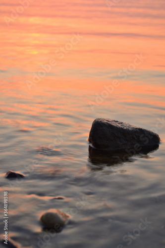 Sea sunset  a large stone in the water in the foreground and against the backdrop of the orange sea and the setting sun.
