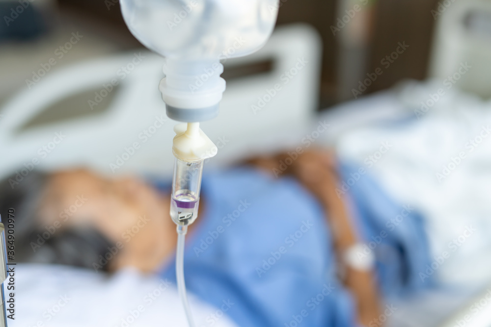 A close-up of a saline bottle strapped to a needle pricked at the hand of a female patient lying in a hospital bed. Medical and treatment of patients concepts A close-up of a saline bottle strapped to a needle pricked at the hand of a female patient lying in a hospital bed. Medical and treatment of patients concepts