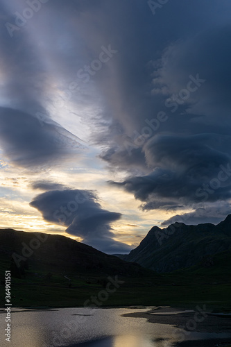 Blea Tarn and The Langdales are silhouetted by cloud formations during sunset in the English Lake District