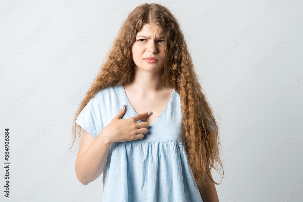 Me?! Portrait of indignant girl with curly long hair startled by offensive words, points at herself with for finger, opens mouth in surprisement, has dissatisfied expression, wears casual clothes Me?! Portrait of indignant girl with curly long hair startled by offensive words, points at herself with for finger, opens mouth in surprisement, has dissatisfied expression, wears casual clothes