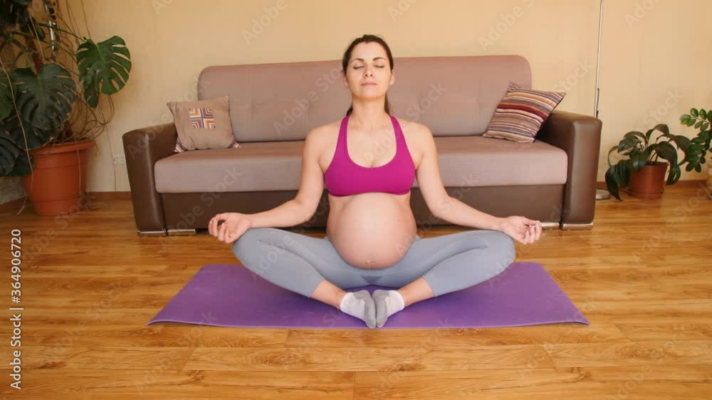 A young pregnant woman does yoga at home. Exercises for pregnant women. Meditation. Bound angle pose. Baddha Konasana. Camera movement.
