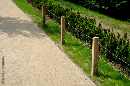 a low fence of land with three steel ropes and wooden poles separates the gravel path from the lawn and the flowerbed with boxwoods in the city park protects against entering the dogs photo