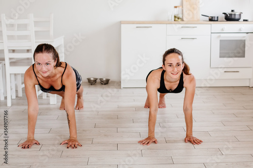 2 girls play sports at home. Two happy girls perform push ups. Fitness in the kitchen. High quality photo