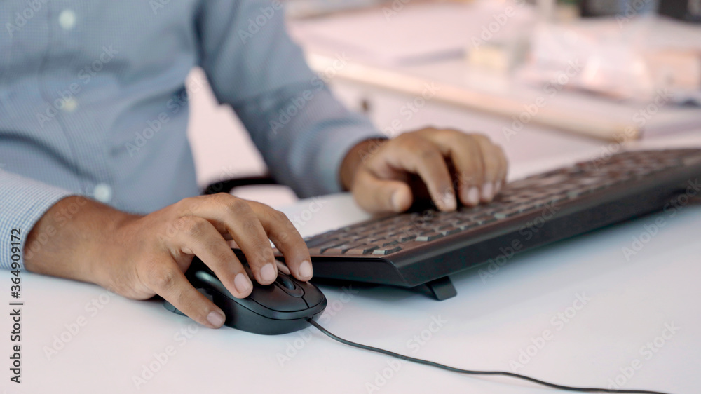Closeup of Indian businessman typing on keyboard and scrolling mouse at desk in office Closeup of Indian businessman typing on keyboard and scrolling mouse at desk in office