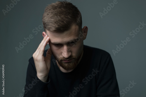 suffering from headache a young bearded guy of about twenty five, in black, presses his hand to his head, suffers from a headache. On a gray background.