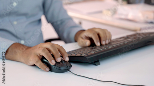 Closeup of Indian businessman typing on keyboard and scrolling mouse at desk in office photo