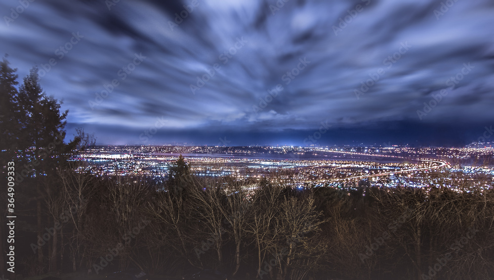 Portland, Oregon Night Cityscape. Fast Moving Clouds. Windy Trees In Foreground. Bright City Lights. Columbia River. Vancouver, Washington in Background.