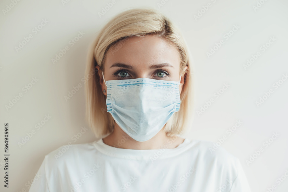 Front view photo of a caucasian woman with blonde hair looking at camera and wear medical mask on face on a white studio background Front view photo of a caucasian woman with blonde hair looking at camera and wear medical mask on face on a white studio background