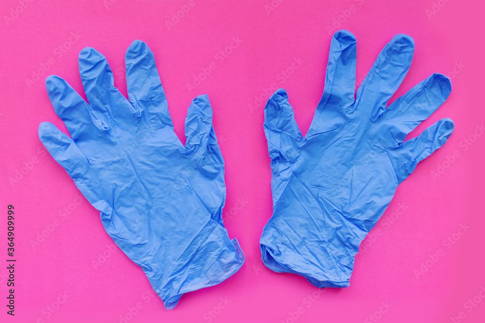 Two blue medical gloves on a pink background. Selective focus.