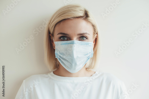 Front view photo of a caucasian woman with blonde hair looking at camera and wear medical mask on face on a white studio background