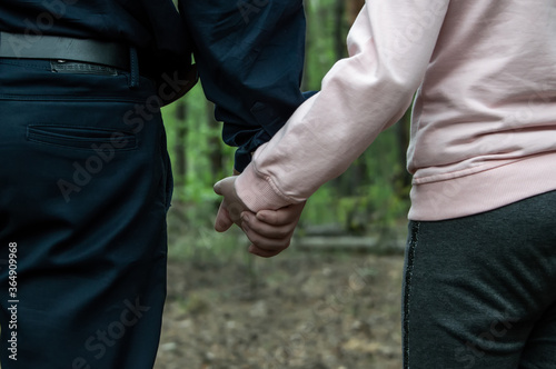 A man holds the hand of a teenage girl in the woods. The concept of kidnapping and child trafficking.